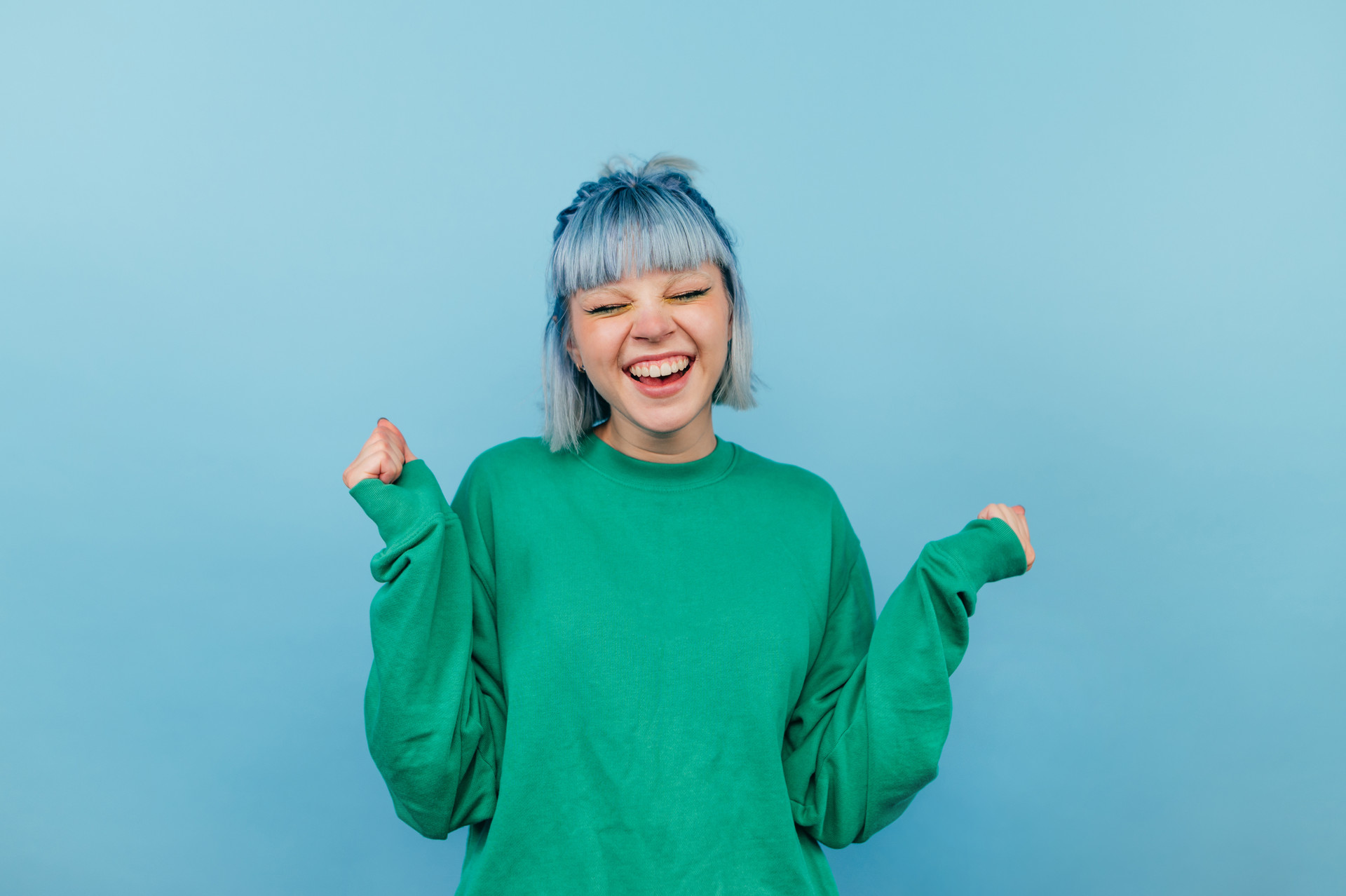 Person mit blauen Haaren lacht vor blauem Hintergrund.