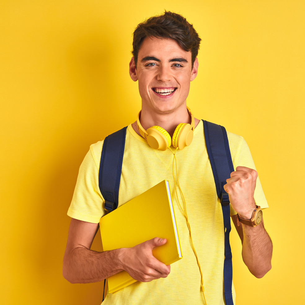 Ein junger Mann mit Rucksack und Notizbuch vor einem gelben Hintergrund.